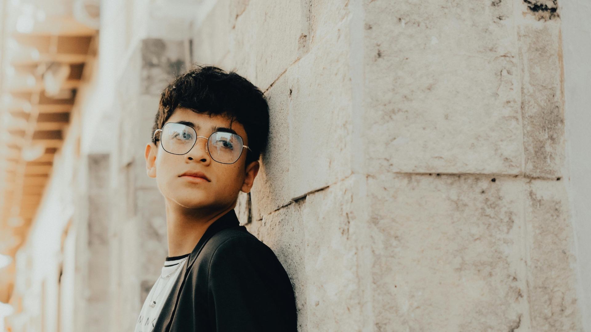 Teen boy leaning against a wall, looking pensive