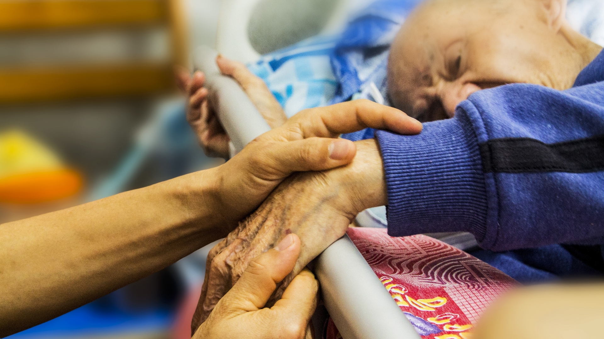Caregiver holding the hand of an elderly patient in bed