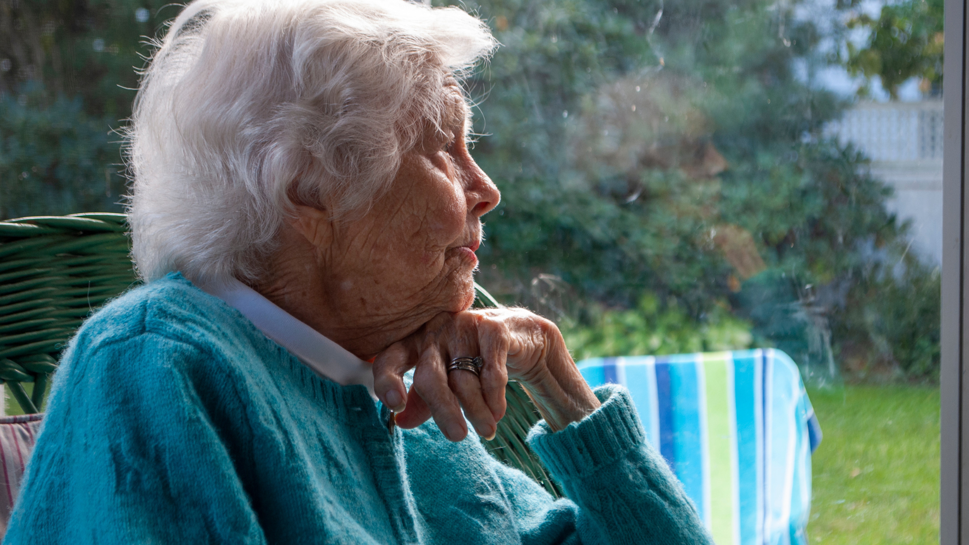 Left Waiting, Left Behind Elderly woman in a teal sweater gazing thoughtfully out a window.
